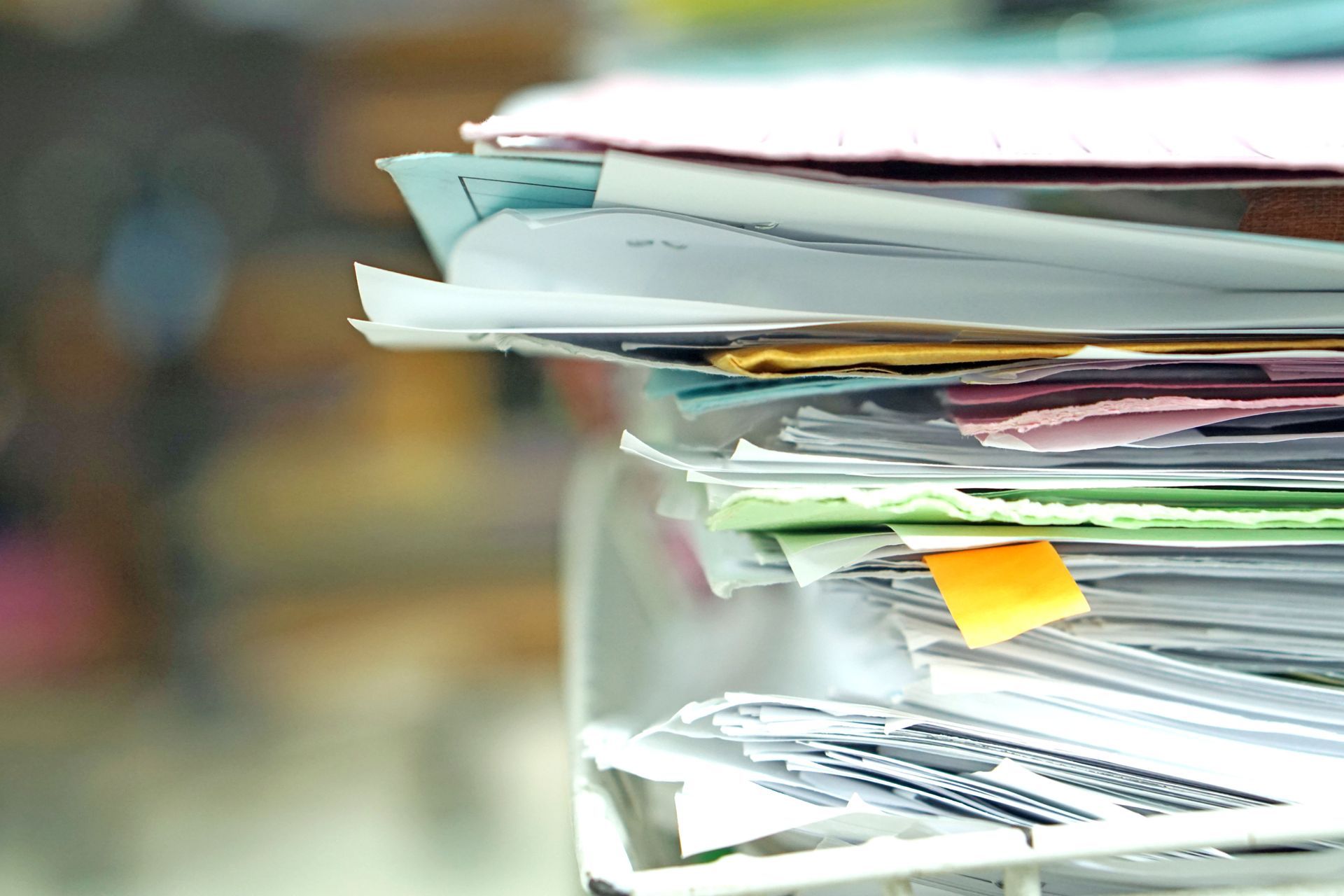 Stack of assorted papers and folders with colored sticky notes on a desk