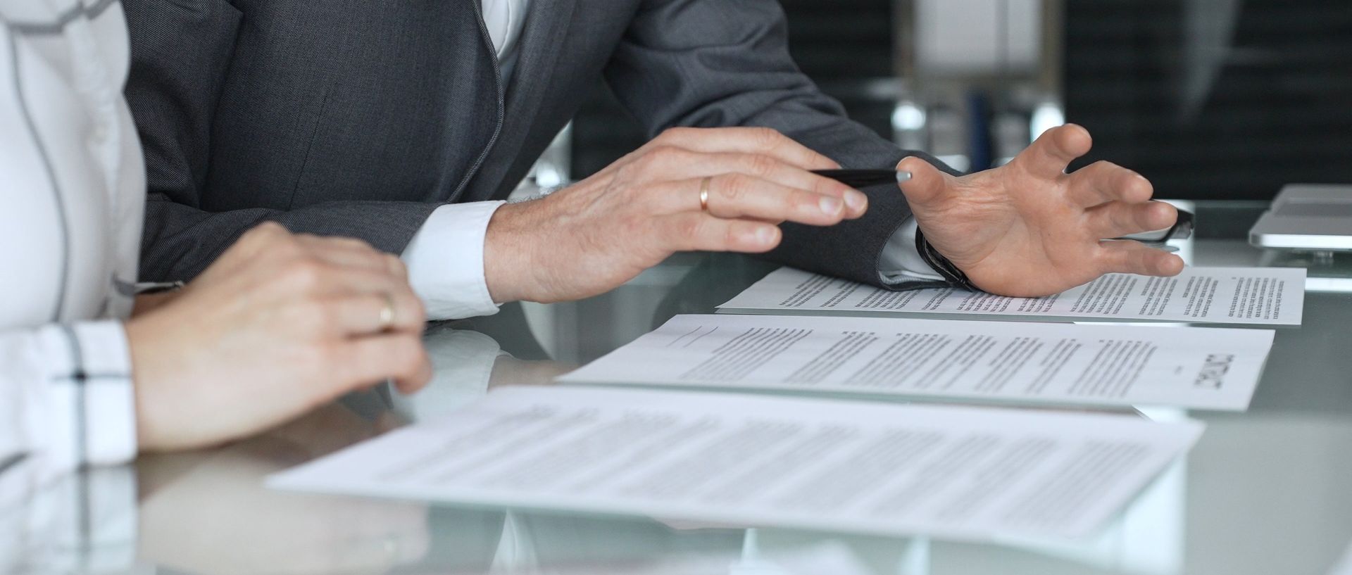 Hands gesturing over documents on a glass table during a business meeting