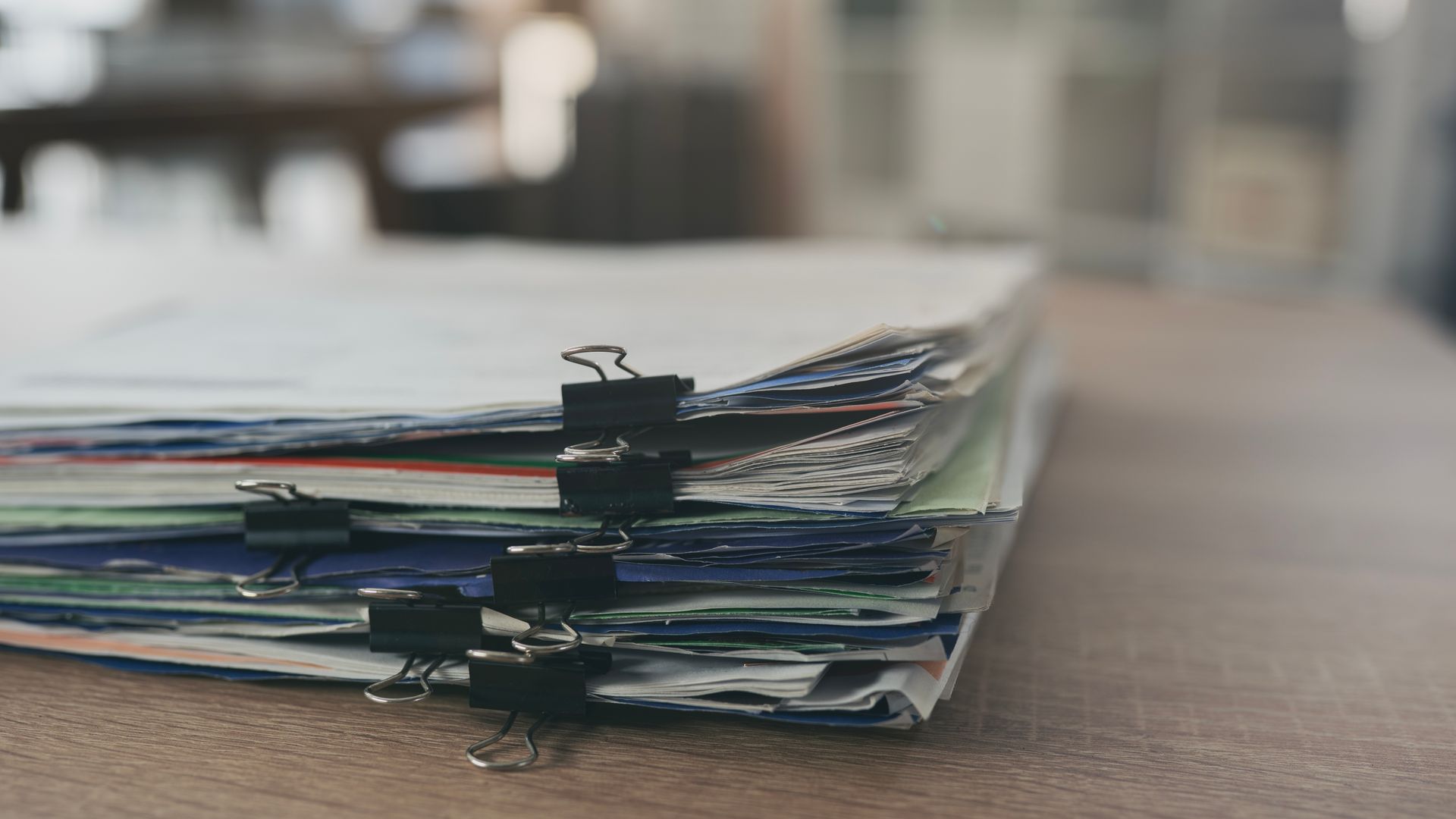 Stack of paper files clipped together on a desk, with a blurred office background