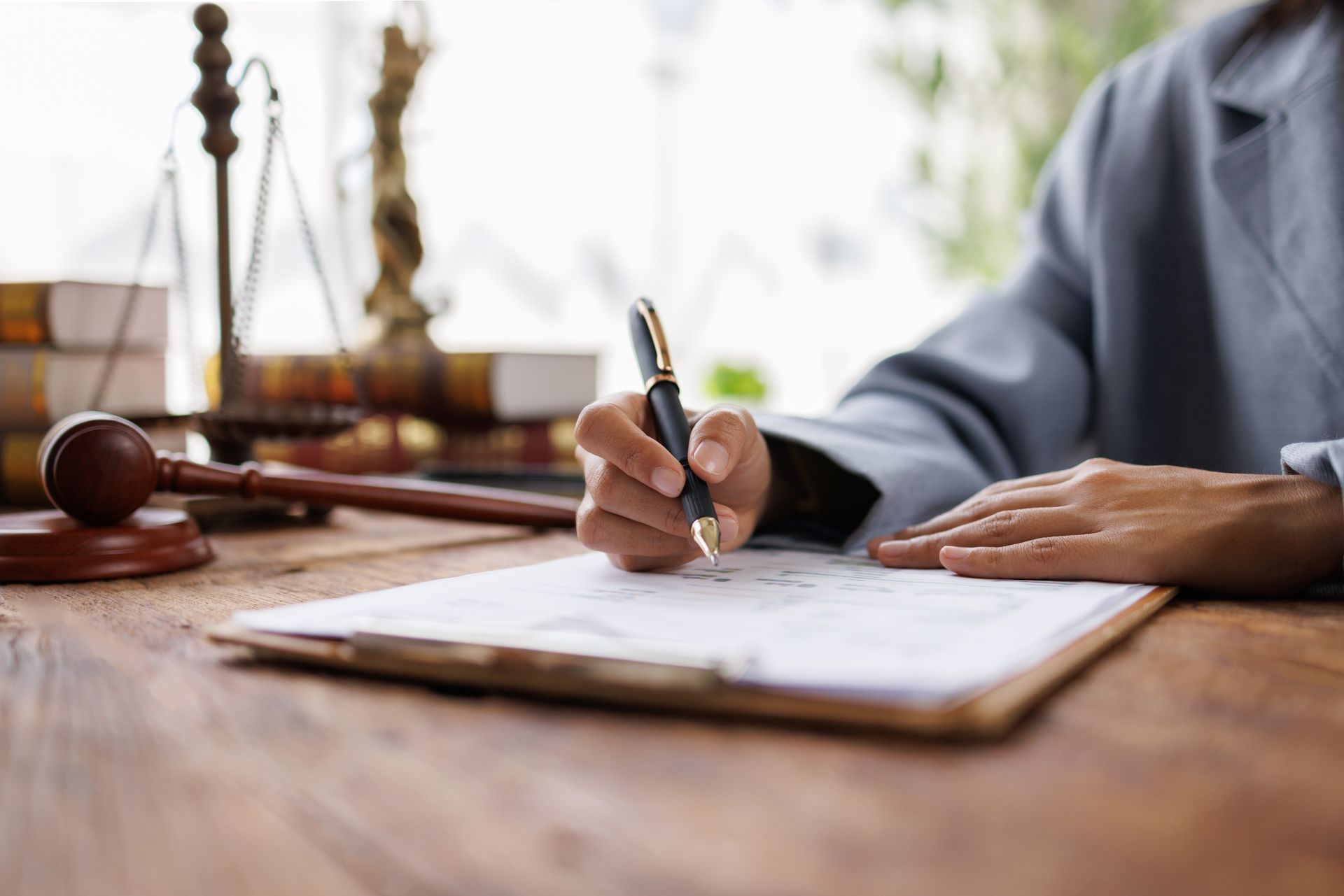 Lawyer signing documents at a desk with a gavel and scales of justice in the background