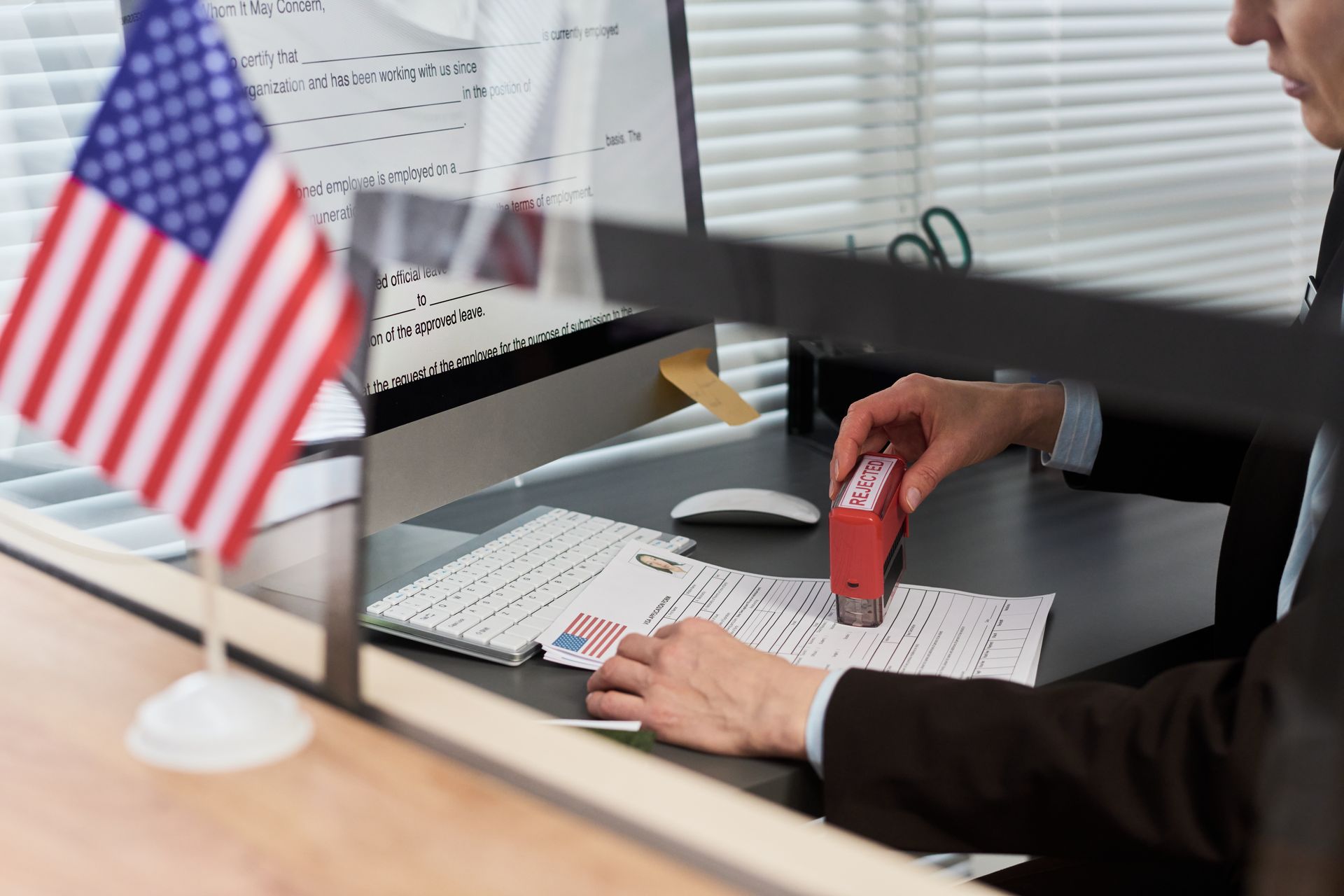 Person stamping documents at an office desk, with a small American flag in the foreground.
