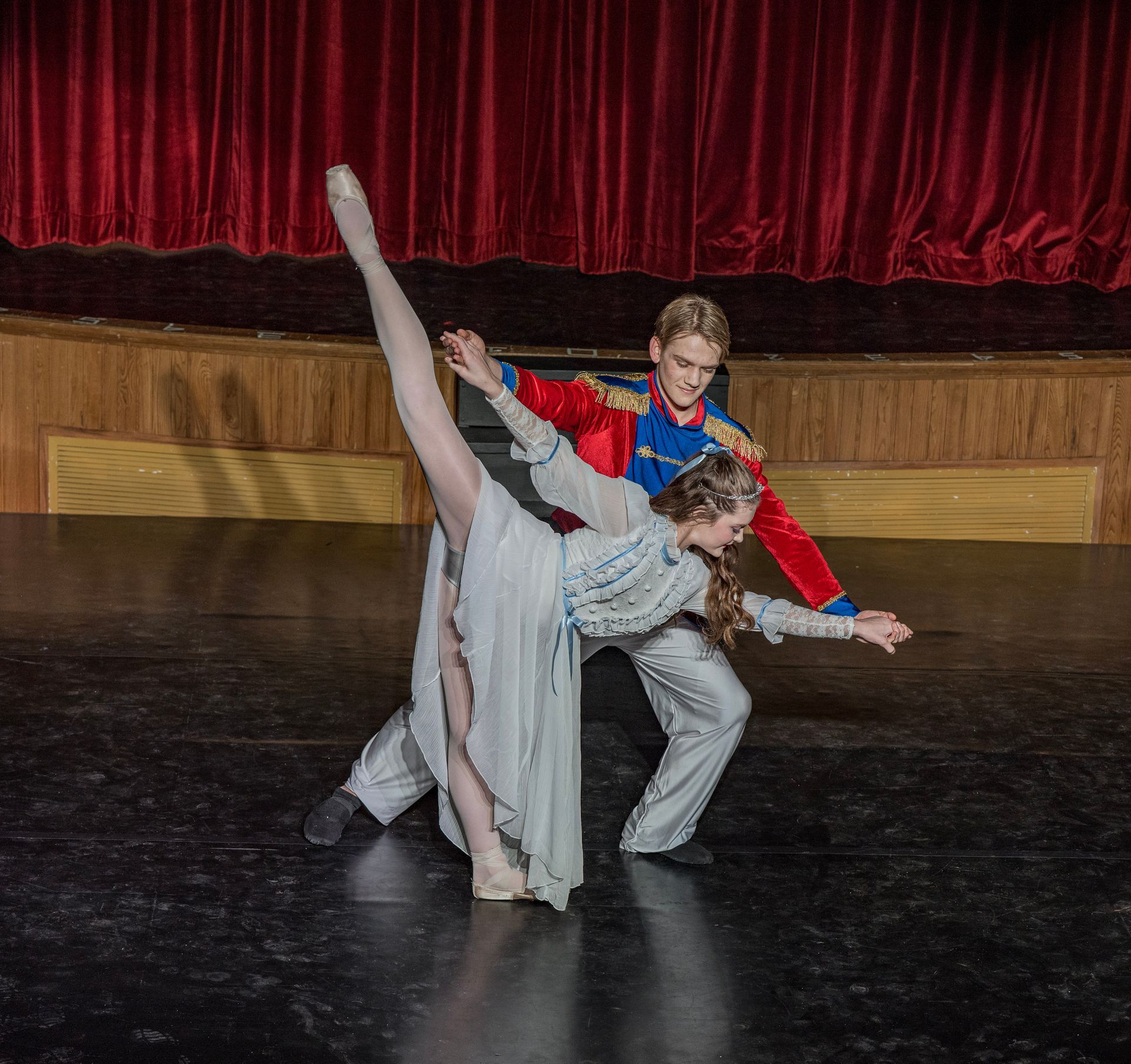 Two dancers in colorful costumes posing in a dramatic lift on a theater stage