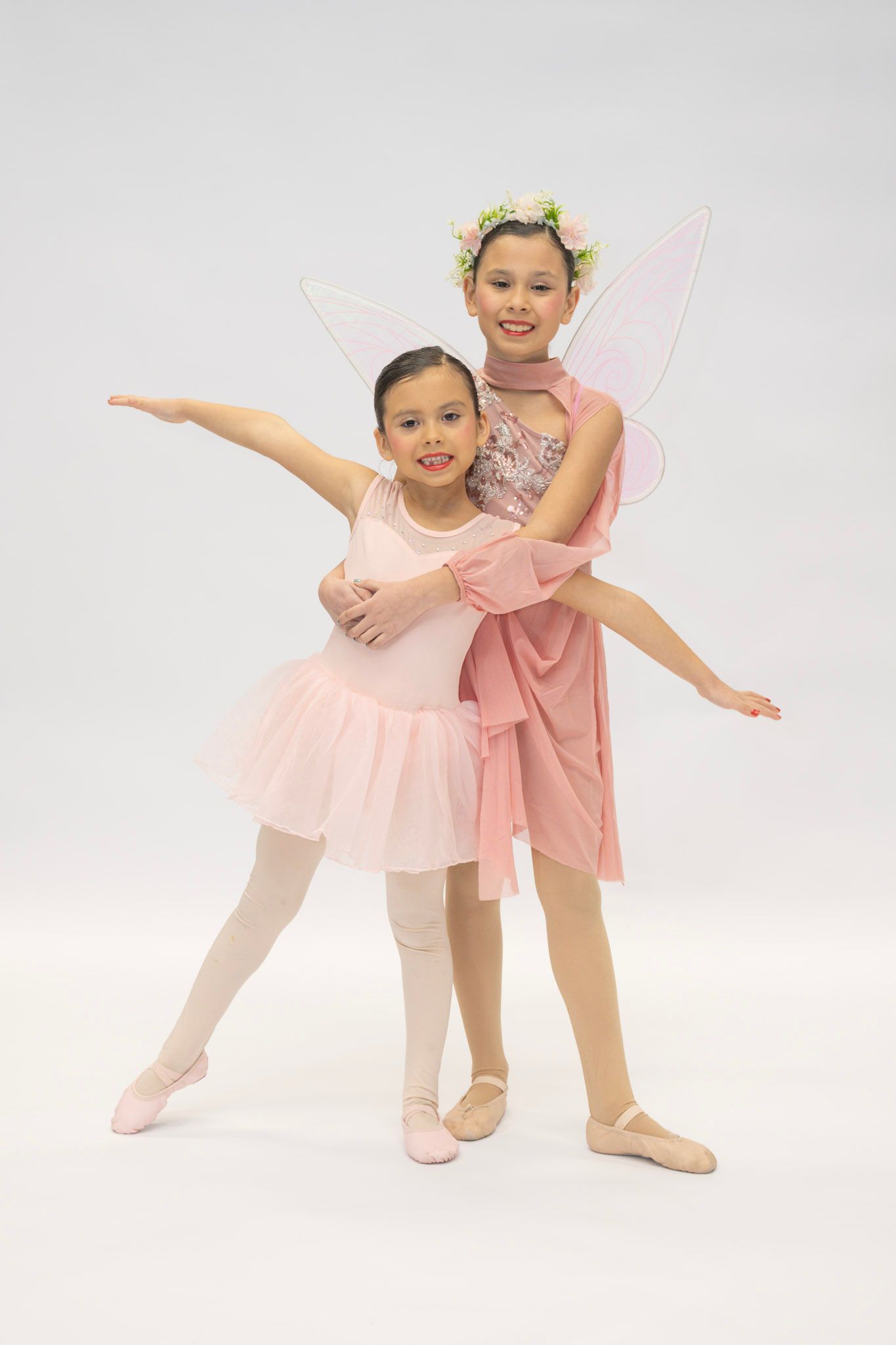 Two ballet dancers in pink tutus posing together against a white backdrop