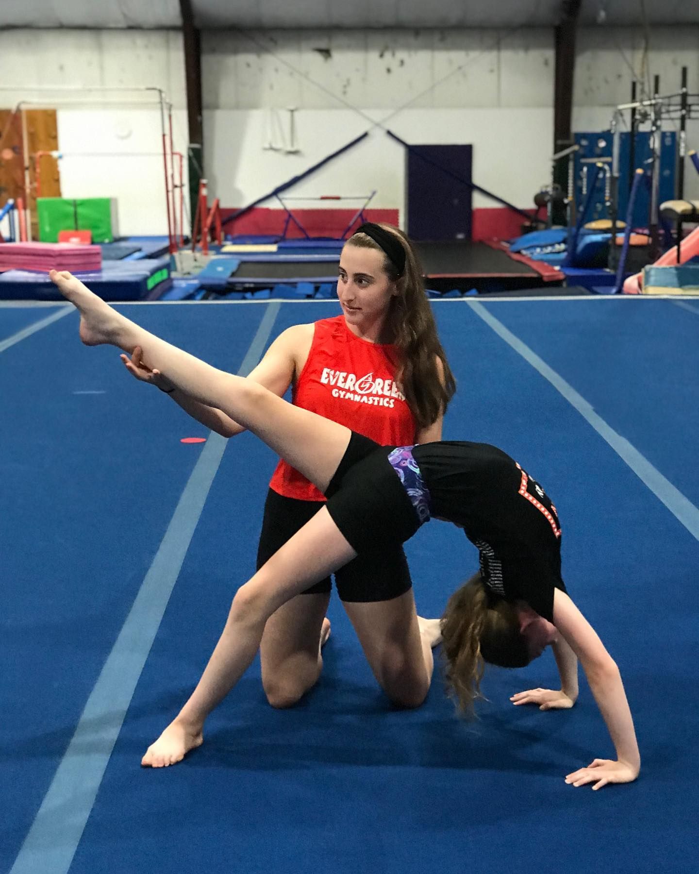 Two gymnasts performing a balance pose on blue mats in an indoor gym