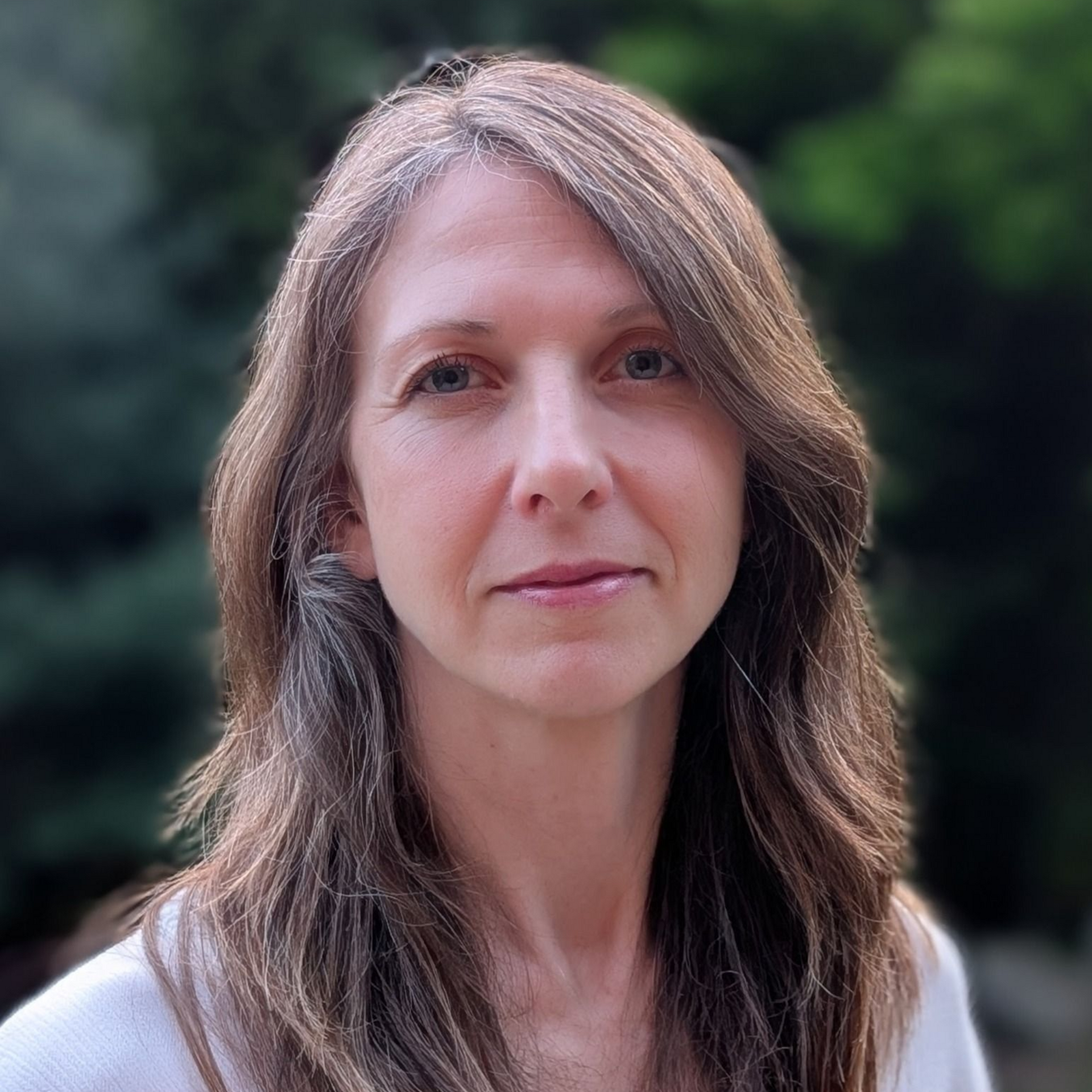 Portrait of a woman with long brown hair against a blurred green outdoor background