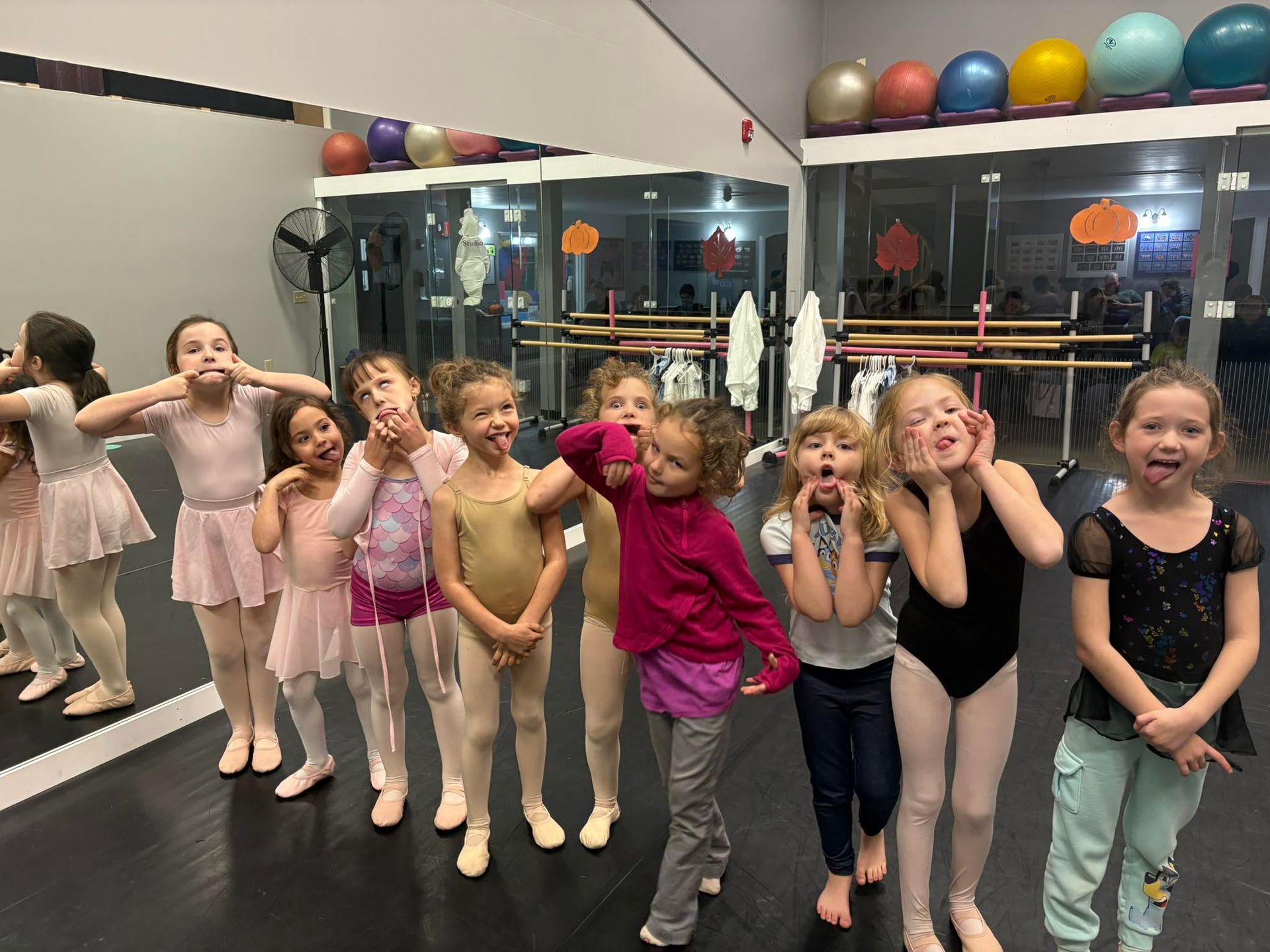 Children in dance attire posing playfully in a studio with mirrors and ballet bars
