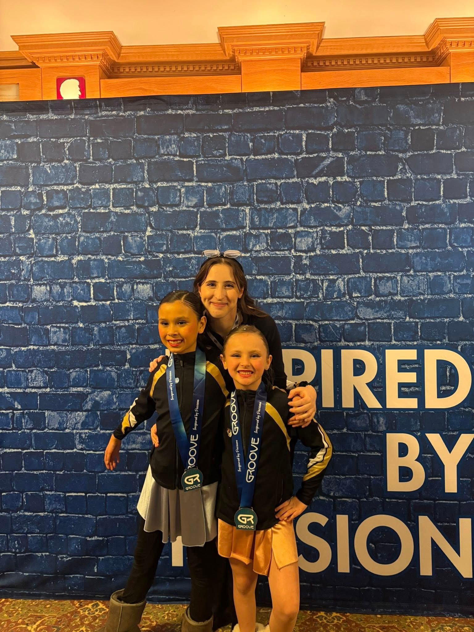 Three people posing in front of a blue brick wall with large “INSPIRED BY” text.