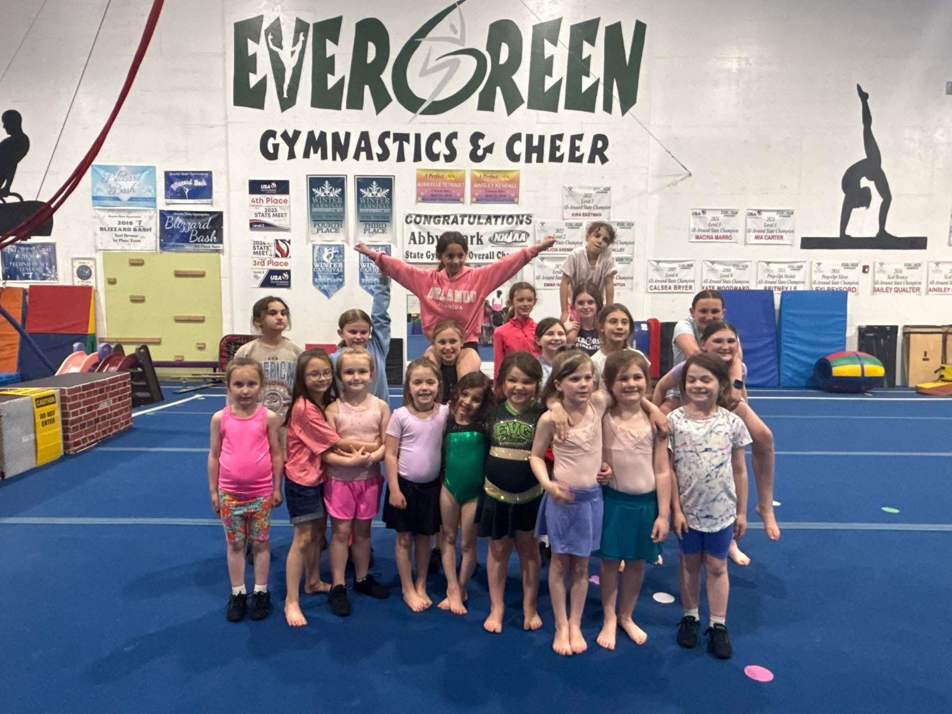 Group of children and an instructor posing in a gymnastics gym under an “Evergreen Gymnastics & Cheer” sign