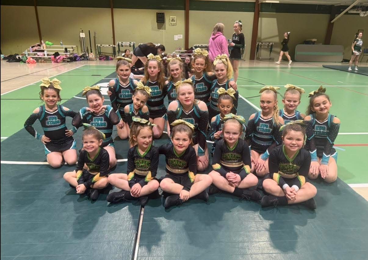 Youth sports team posing on a gym floor, wearing matching black and teal uniforms, smiling in three rows.