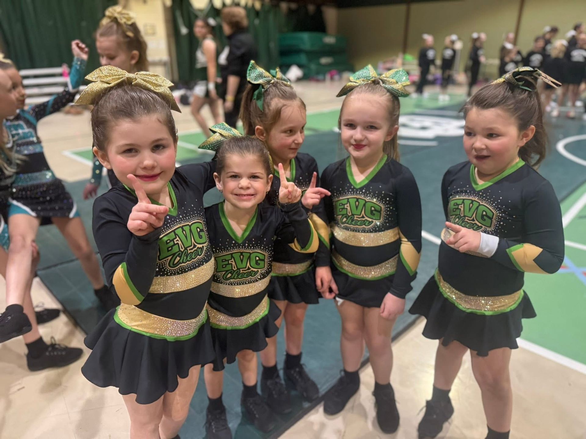 Five young dancers in black and gold costumes smiling and posing together indoors.