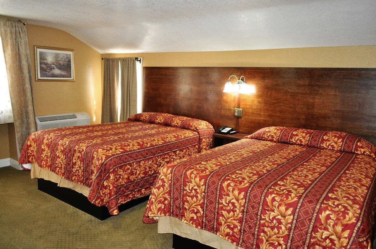 Two double beds in a motel room with patterned red bedspreads, brown headboards, and a beige wall.