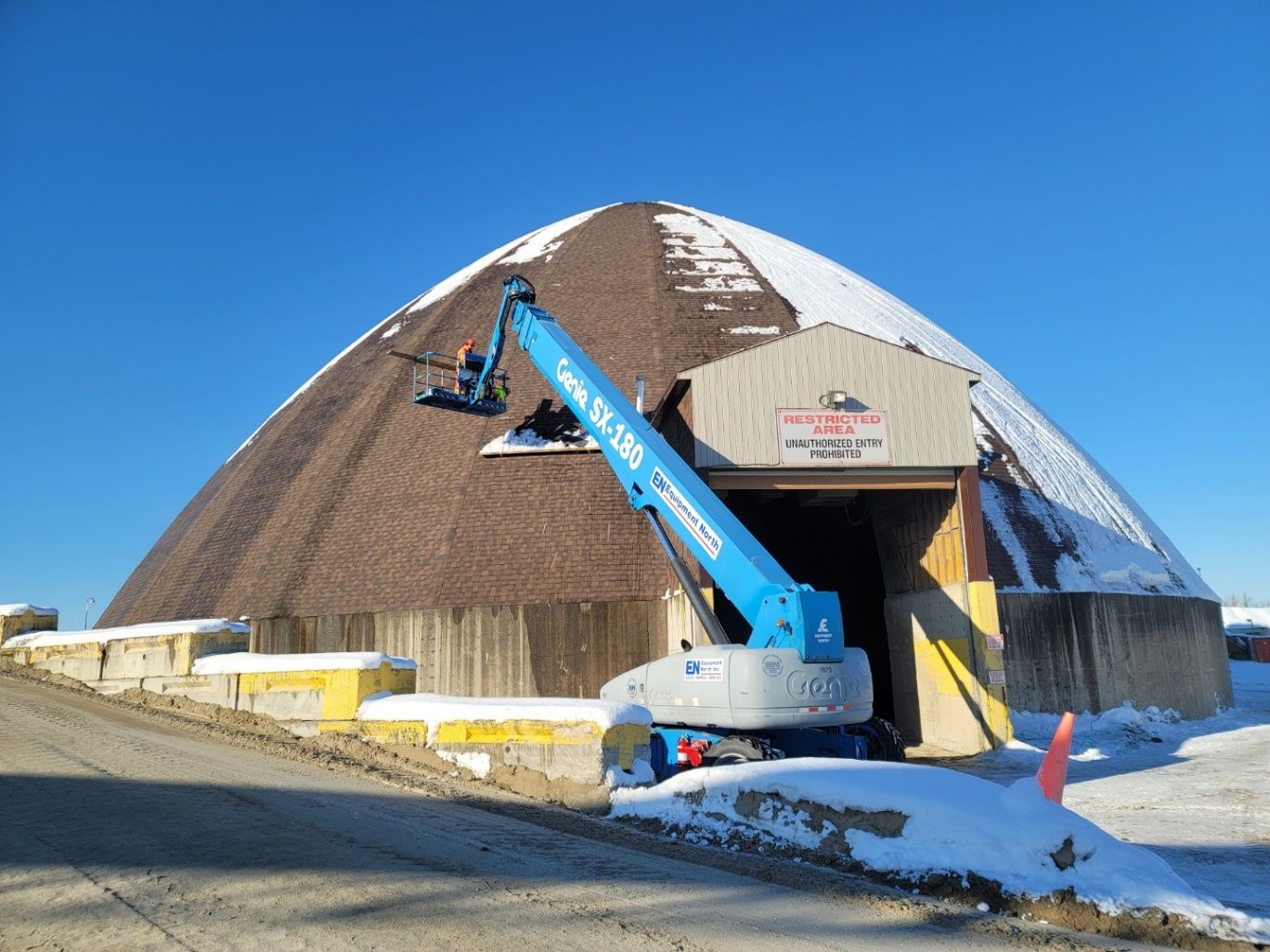 Blue boom lift working on a dome-shaped building with snow on the ground under a clear sky