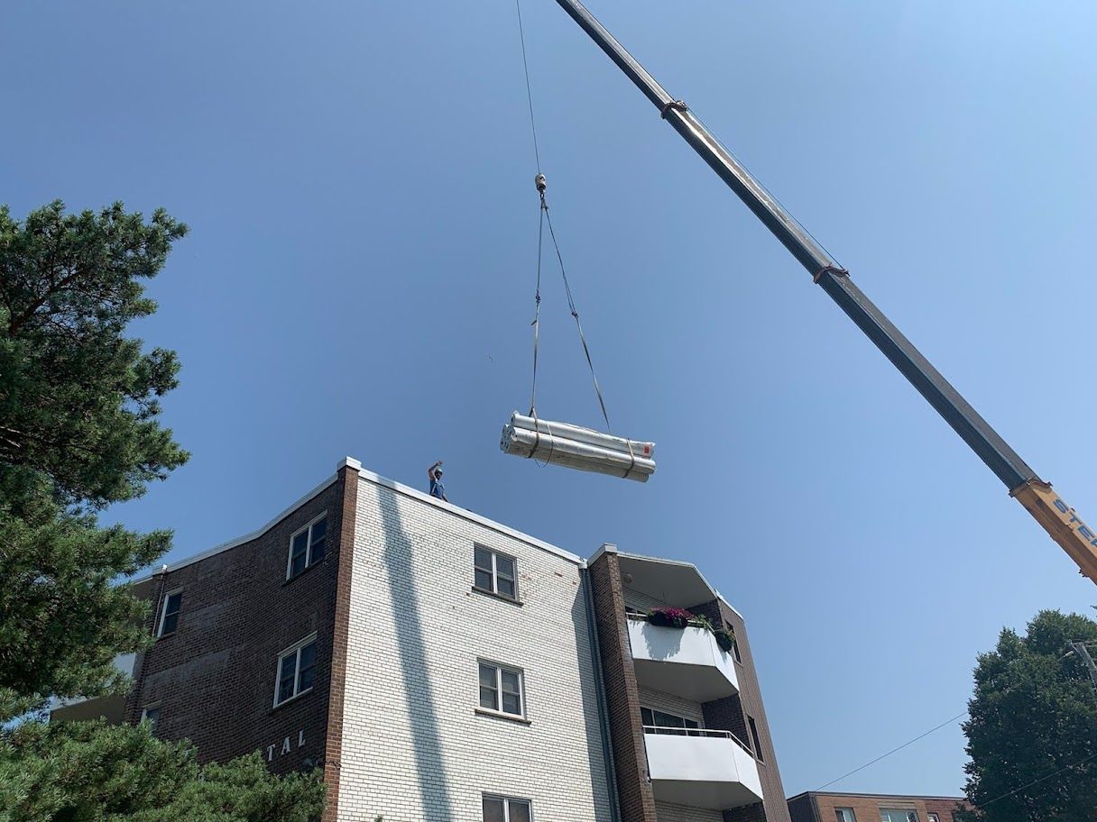 Crane lifting a long beam above an apartment building under a clear blue sky