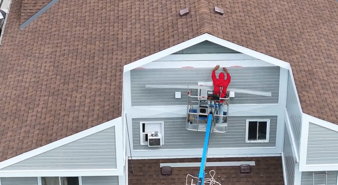 Person on a lift working on the siding of a building with brown roofing.