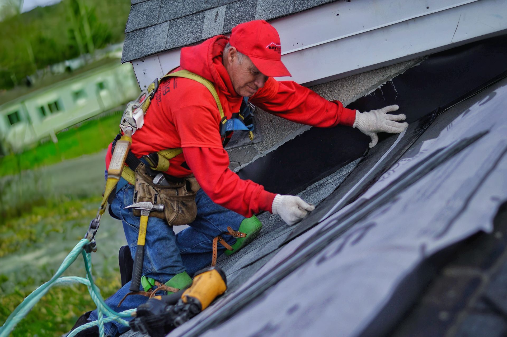 Roofer in red jacket and hardhat installing roofing material on a sloped roof.