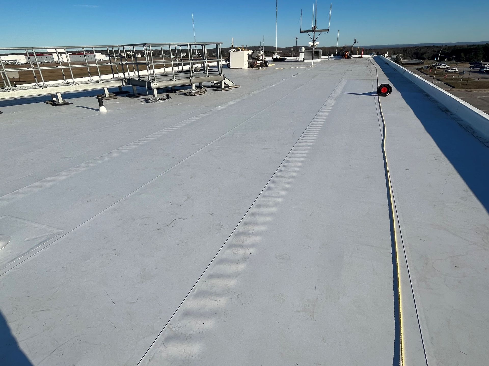 Snow-covered rooftop with a safety line and distant city skyline under a clear blue sky