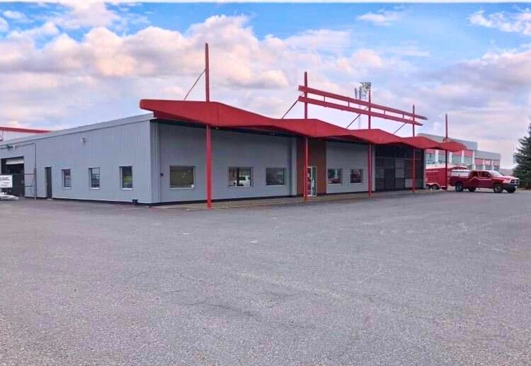 Gray commercial building with red awnings and a large parking lot under a cloudy sky