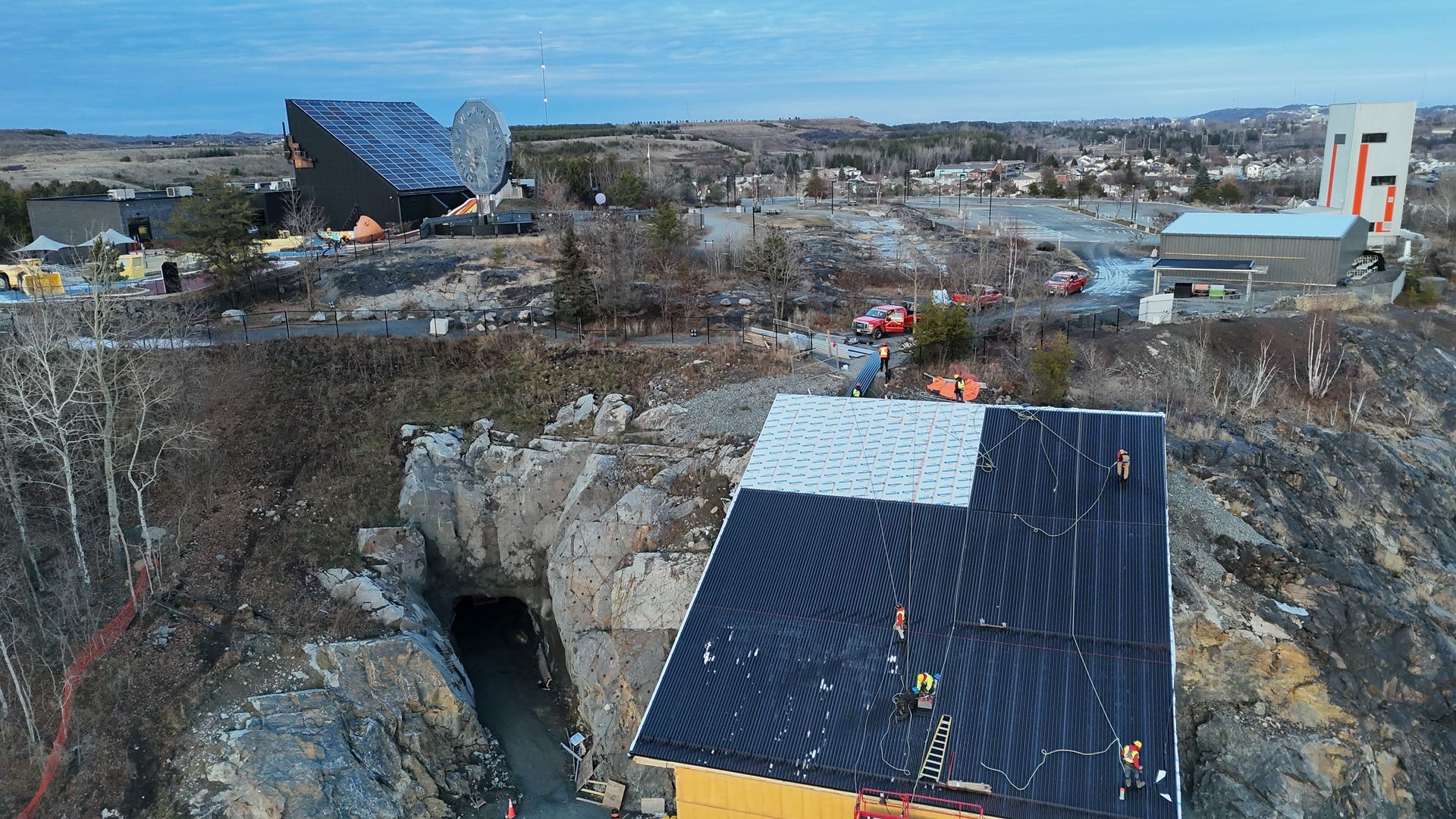 Rocky landscape with a cave opening, a small building, and a distant modern structure under a clear sky
