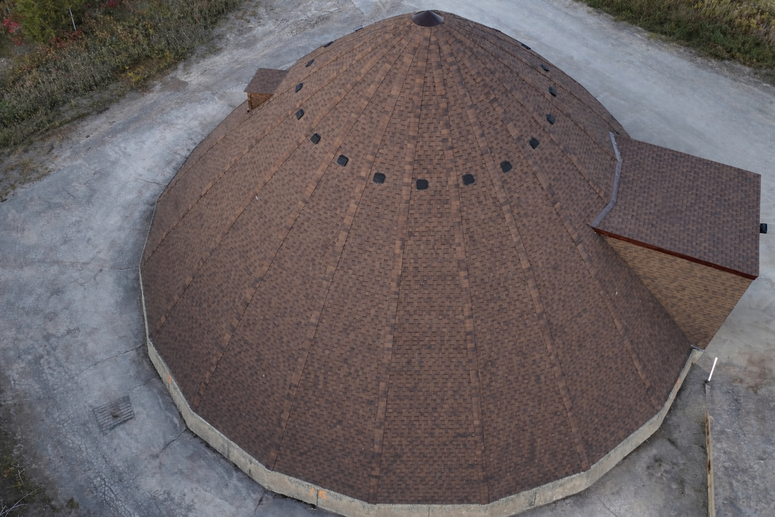 Aerial view of a round brown-roofed building with a small attached entrance