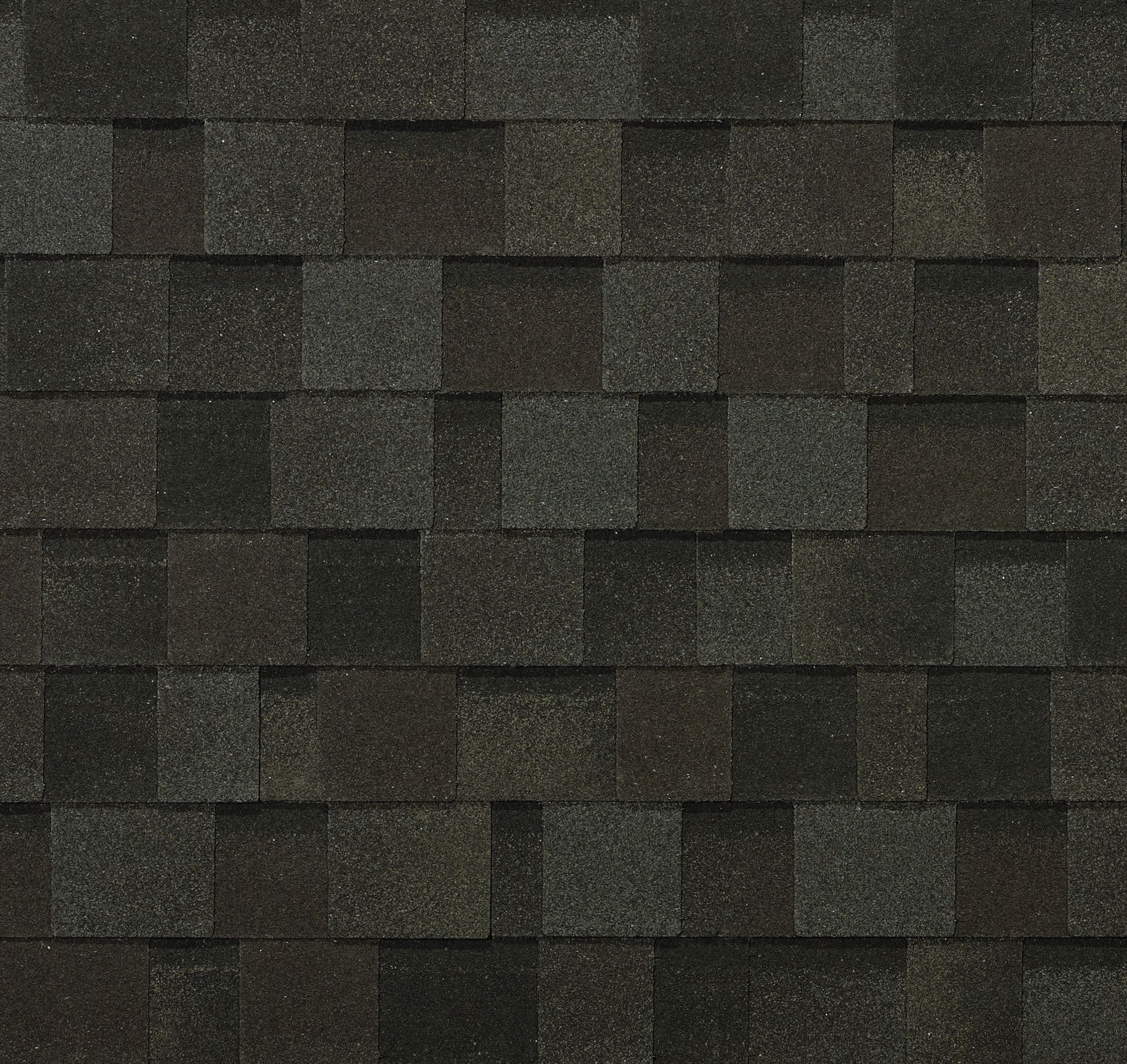 A close-up view of dark, charcoal-colored asphalt roofing shingles with a textured, multi-layered pattern.