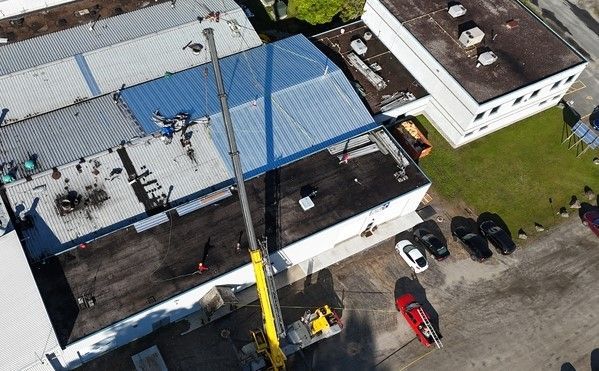 Aerial view of a building roof being repaired with a crane and workers nearby