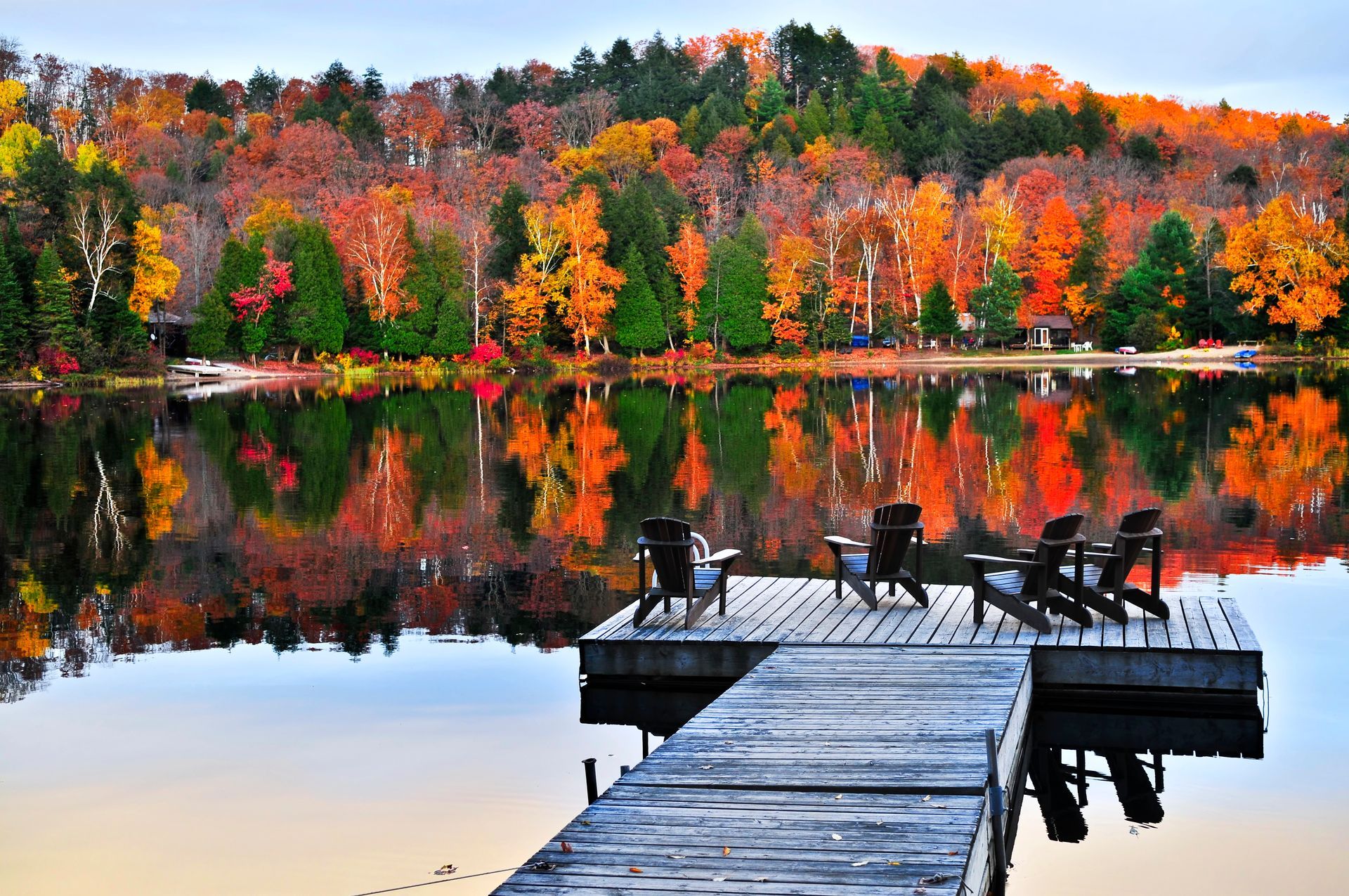 Autumn lake with colorful trees and a dock with chairs reflecting in still water