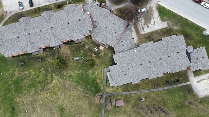 Aerial view of two gray-roofed houses beside a large grassy yard and driveway.