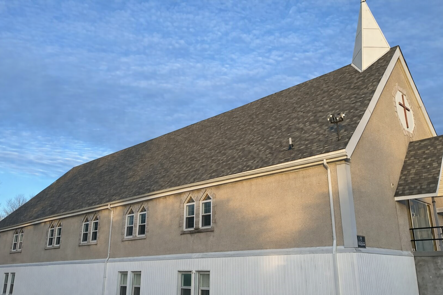 Beige church building with a steep dark roof and white trim against a blue sky