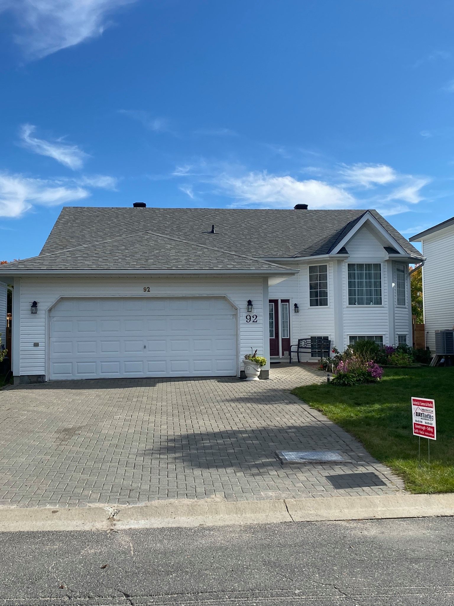 Suburban house with attached garage, gray roof, white siding, and a paved driveway under a blue sky