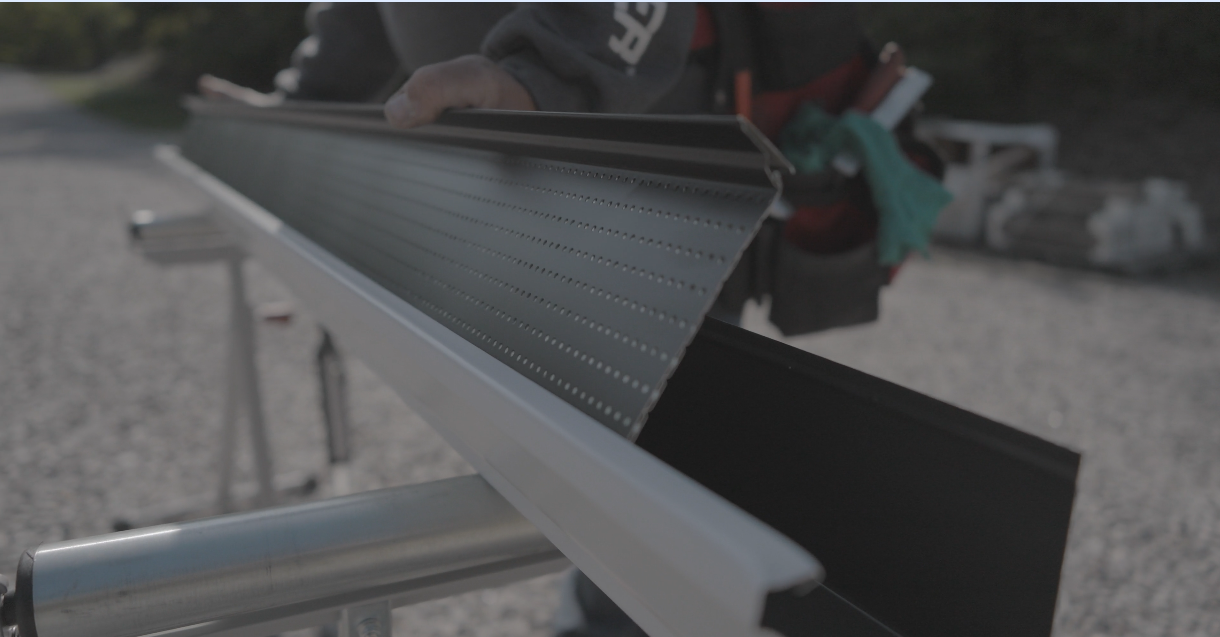 Person installing black gutter guard onto white gutter, outdoors.