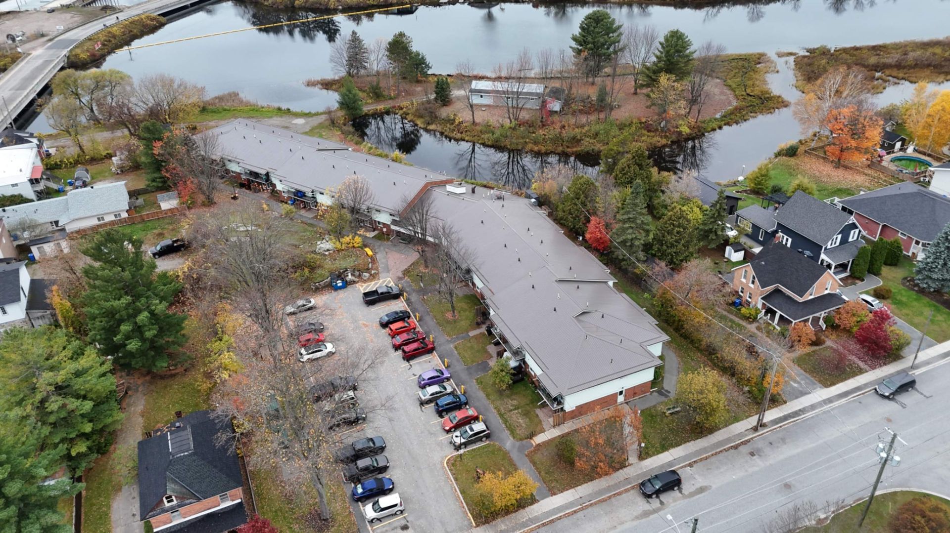 Aerial view of apartment buildings, parked cars, and flooded roads beside a river in autumn.