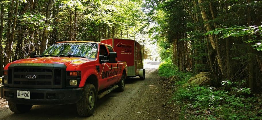 Red truck towing a trailer on a forest road