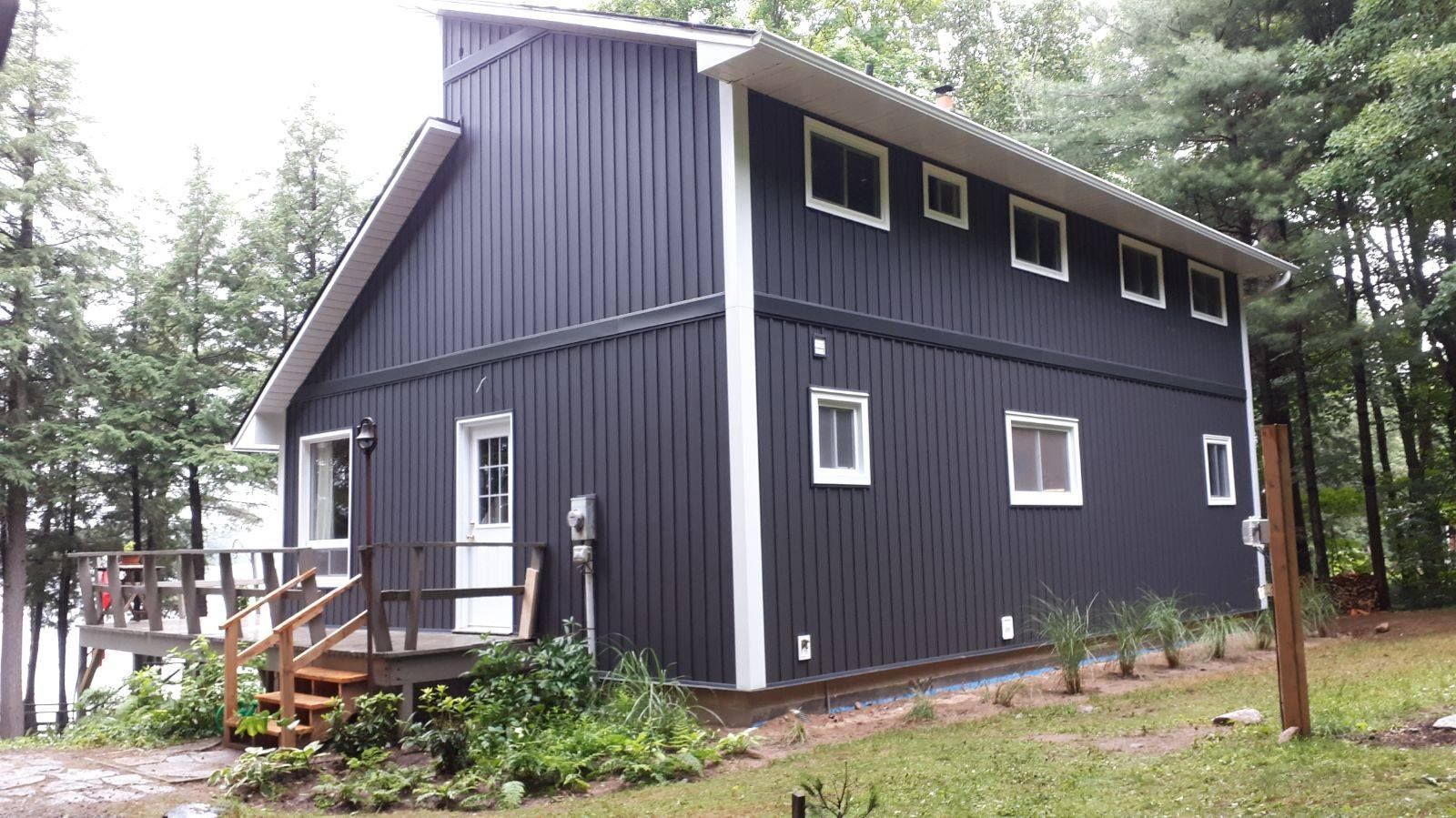 Dark gray house with white trim and a small porch, surrounded by trees and greenery