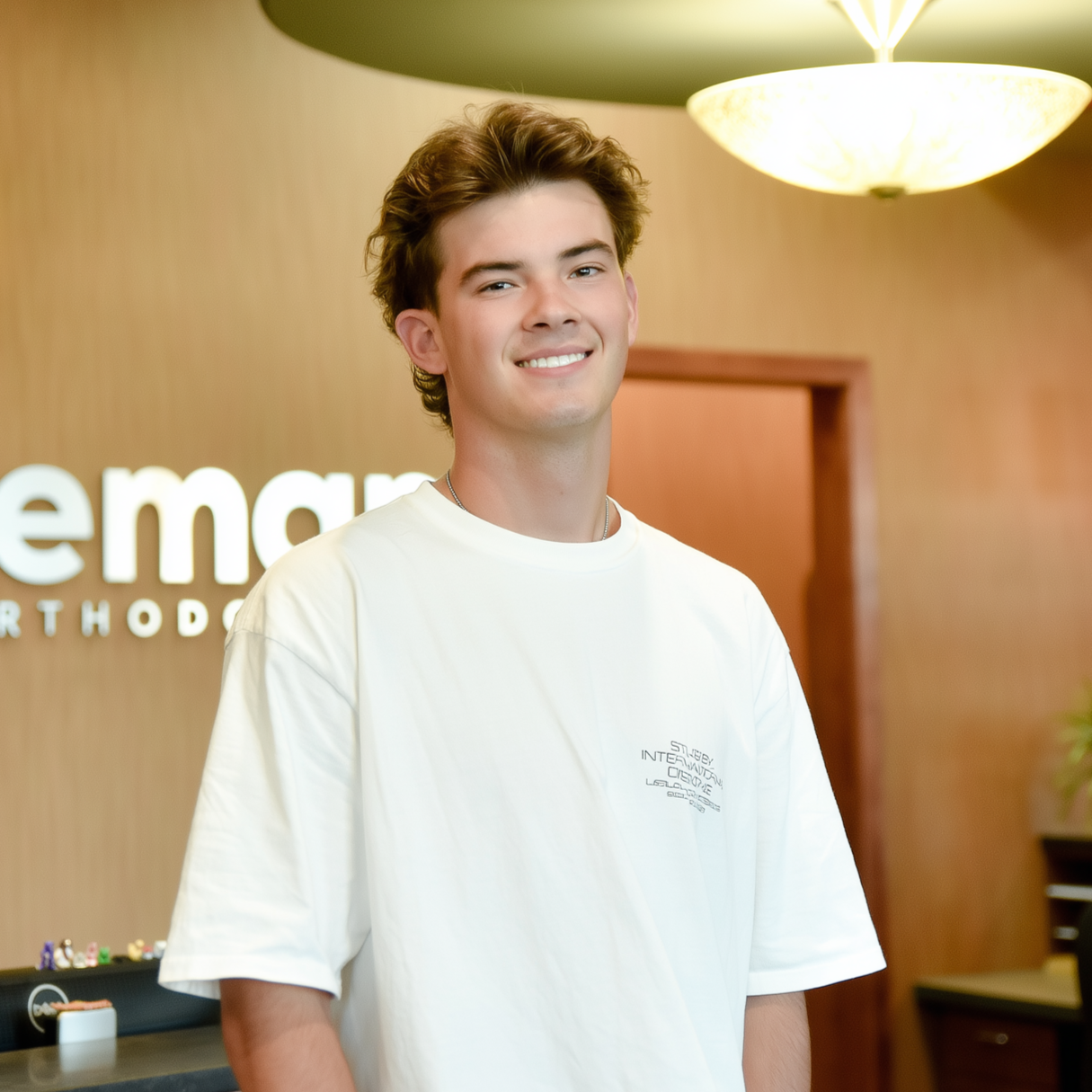 Man in white shirt smiles in front of a dental office reception desk.