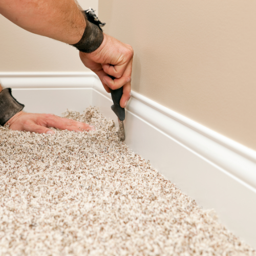 A person is laying carpet on the floor in a room