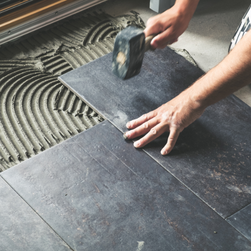 A person is laying a tile floor with a hammer.