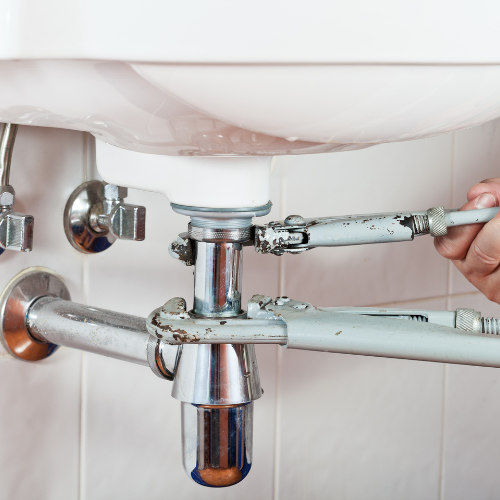 A person is fixing a sink with a wrench.