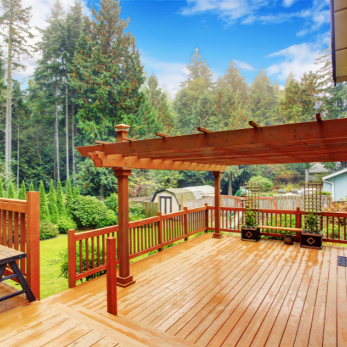 A wooden deck with a pergola and trees in the background