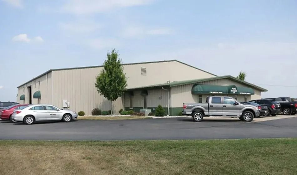 A beige industrial building with green awnings and parked cars in the foreground on a sunny day.