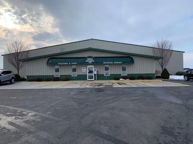 A single-story warehouse building with beige siding, a green metal roof, and a central entrance with a green awning.