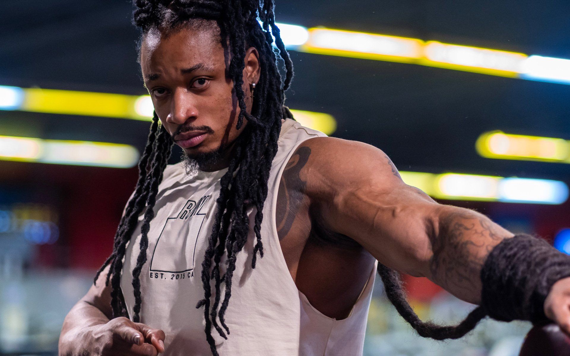 Athlete in white jersey with long dreadlocks, reaching forward in a stadium with blurred lights.