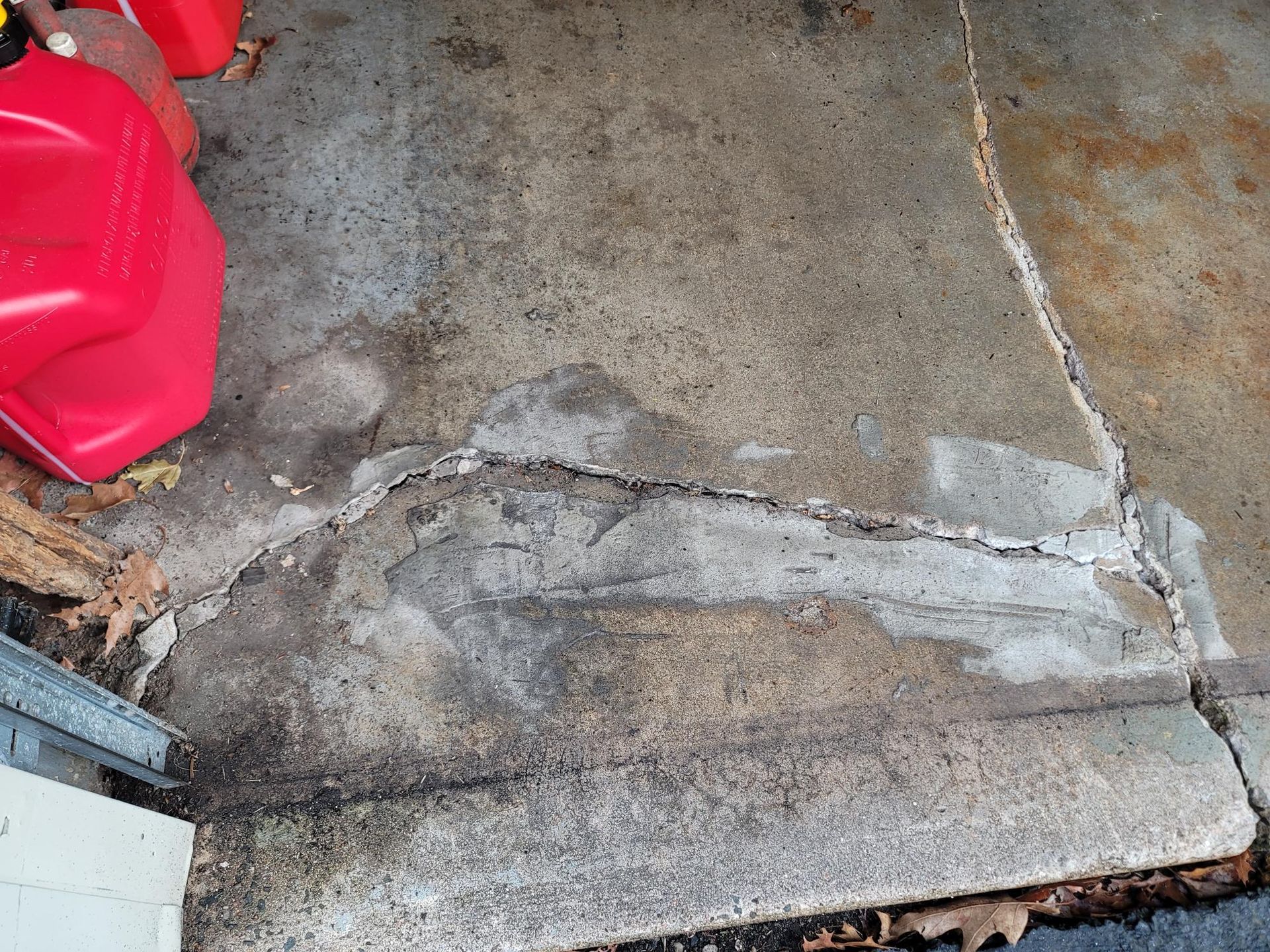 Cracked concrete driveway with a large, filled crack near the garage door. Red gas can sits nearby.