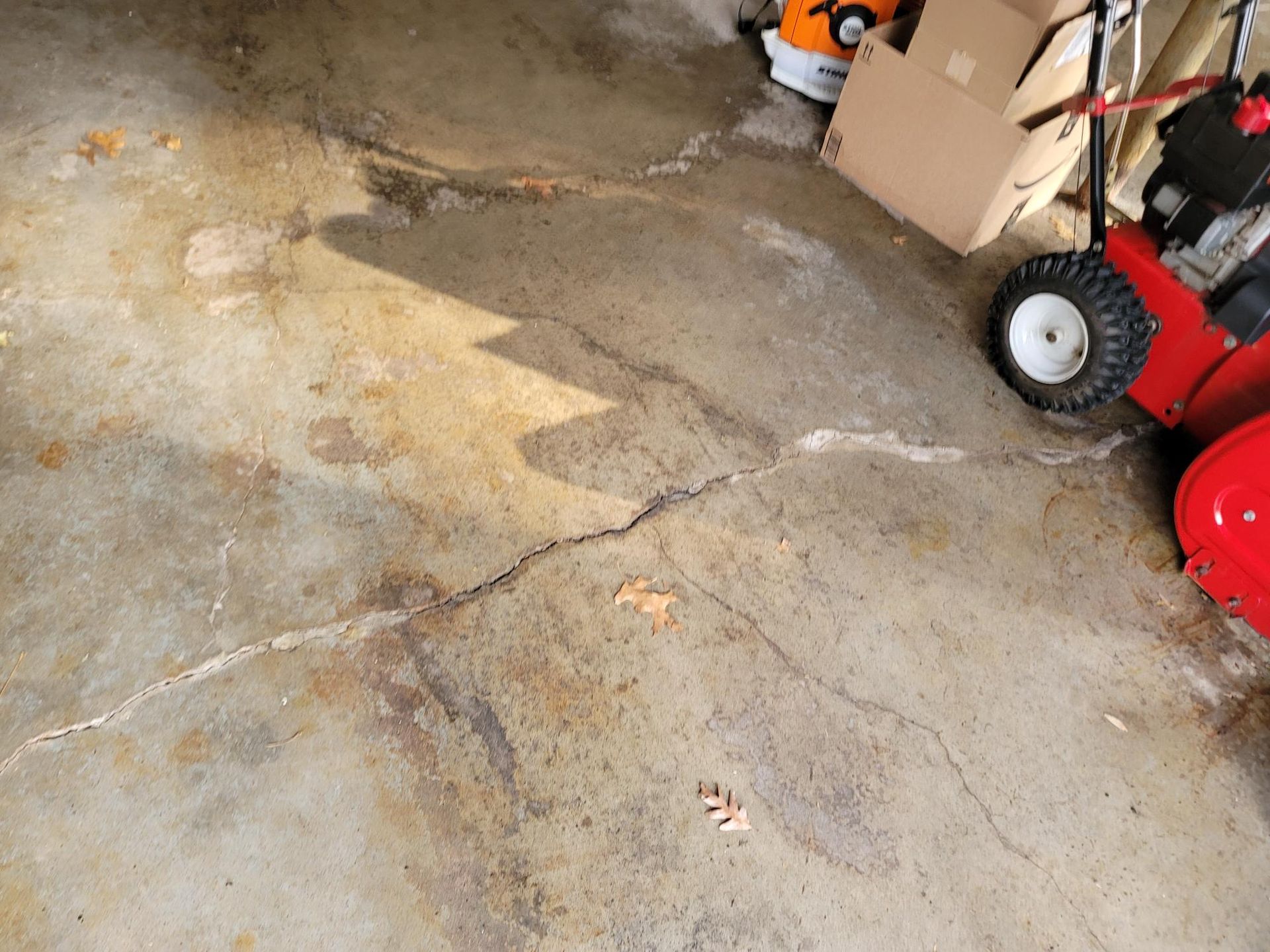 Cracked, stained concrete garage floor with a snowblower, box, and other items.