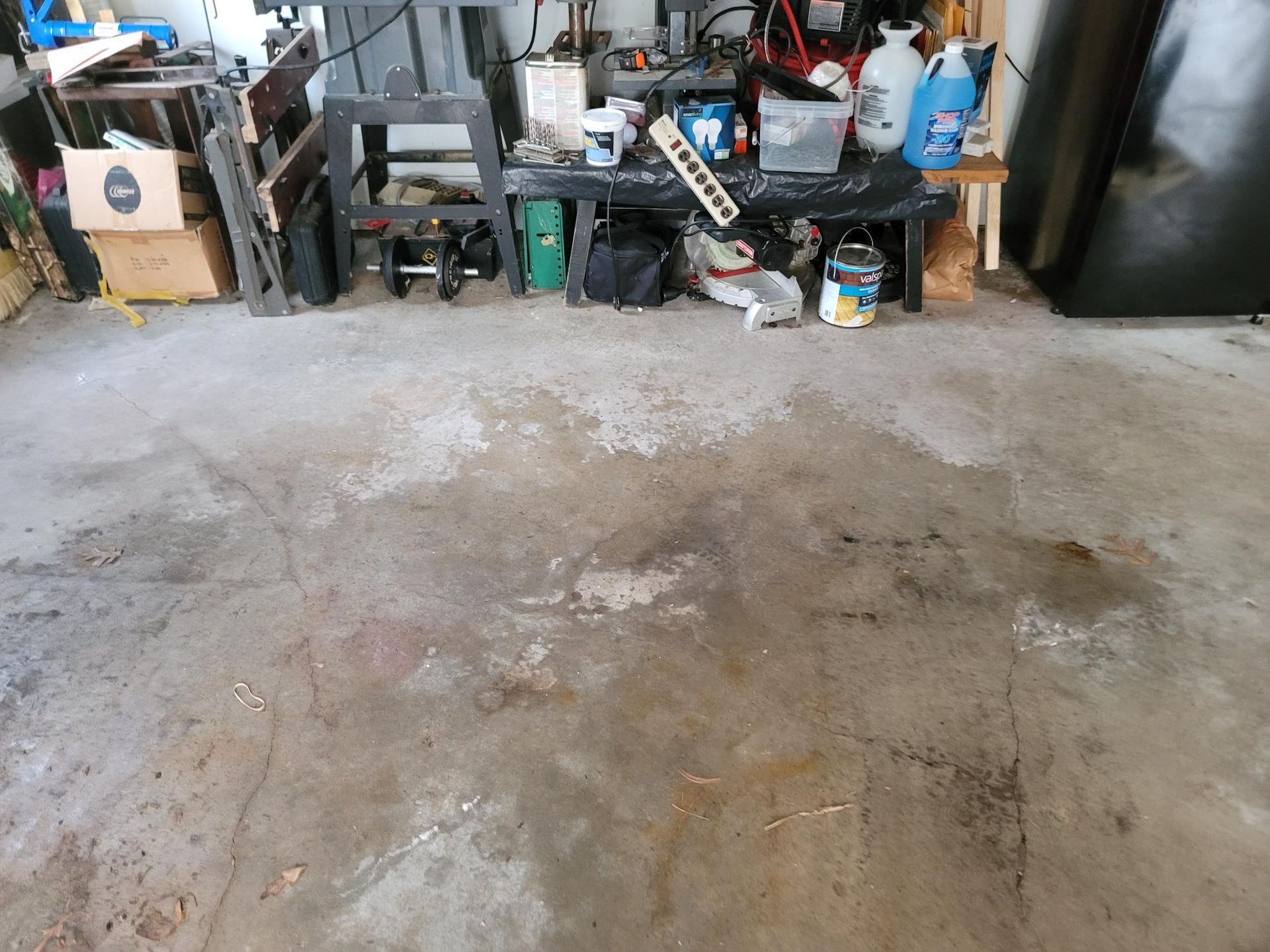 Concrete garage floor with stained areas, cluttered work area in the background.