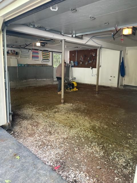 Garage under construction; gravel floor, walls, and support beams. Person operating a compactor. Garage door open.