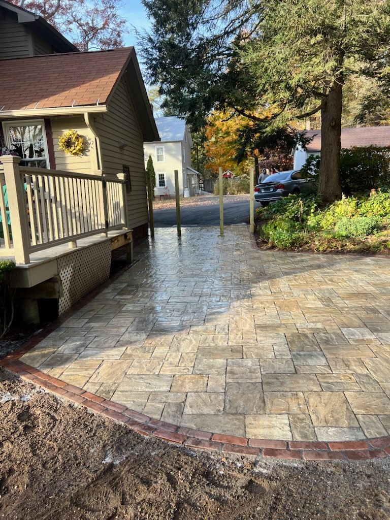 Brick patio with brown pavers, leading to a home with a wooden porch.