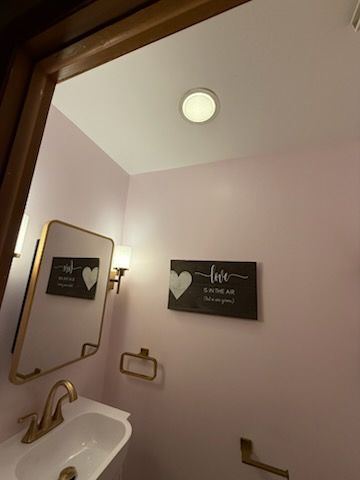 Pink bathroom with gold fixtures and decor: mirror, faucet, towel ring, and a wall art.