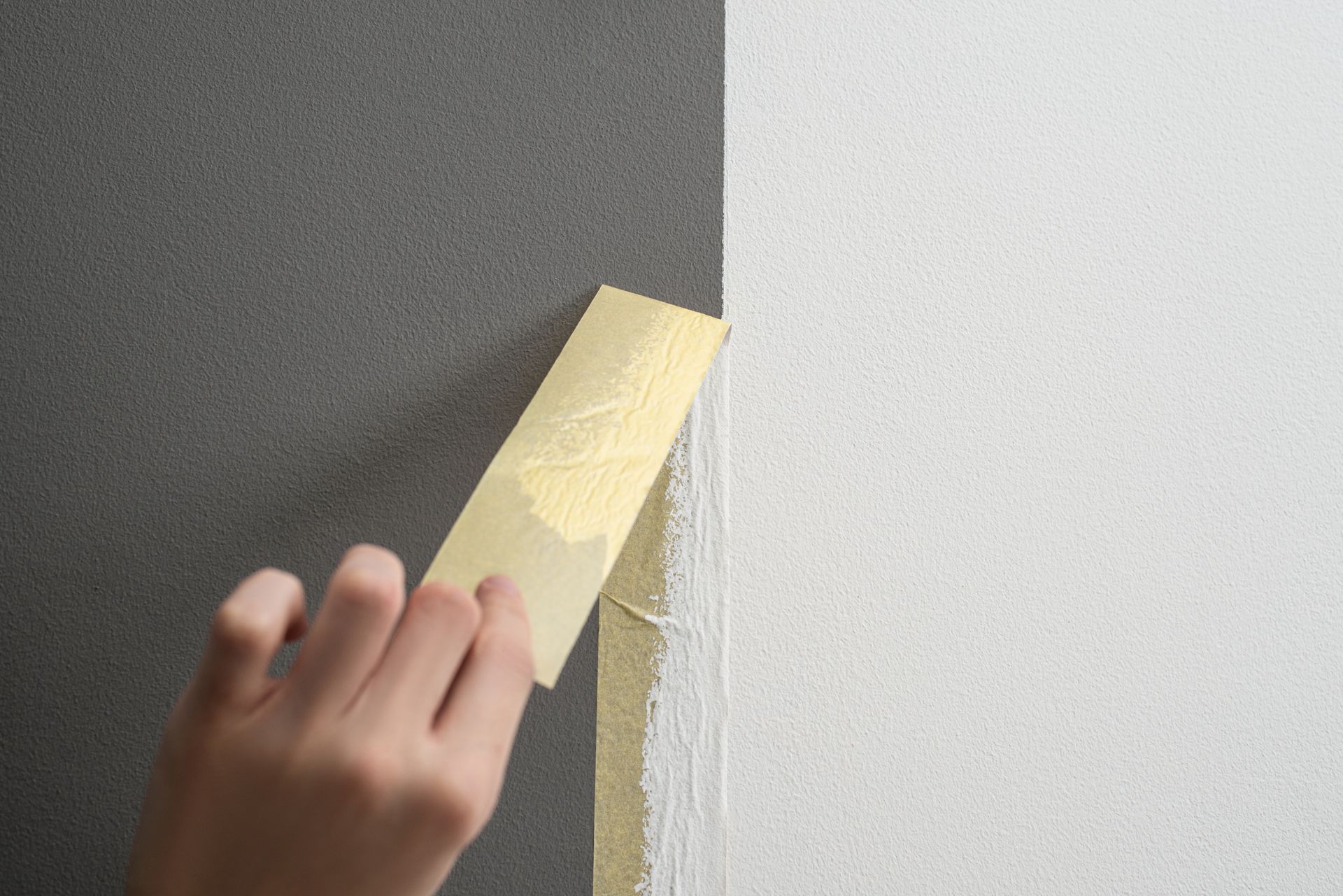 A person is peeling off a piece of tape from a wall.