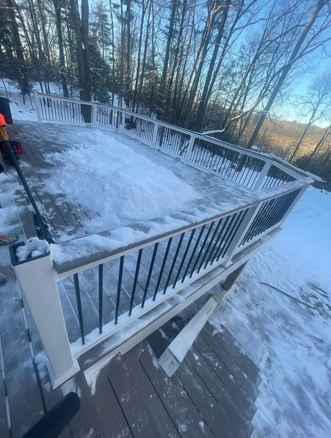 A snowy deck with a railing and trees in the background.