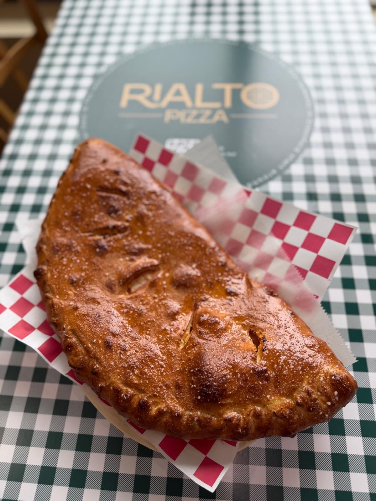 Calzone on checkered paper in basket, Rialto Pizza sign in background.